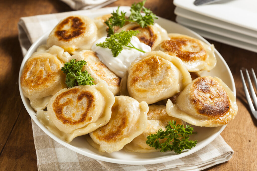Hausgemachte polnische Pierogi mit goldbrauner Kruste, Sauerrahm und Petersilie auf einem Teller.