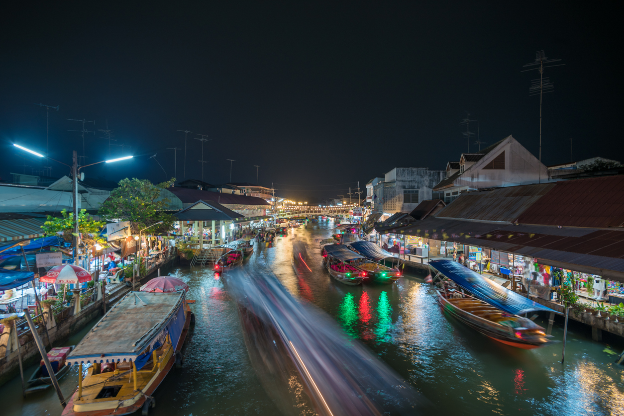 Boote fahren bei Nacht durch den beleuchteten Kanal am Amphawa Floating Market in Thailand.