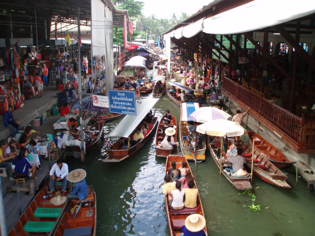 Auf einem engen Kanal fahren viele Boote zwischen Marktständen und bunten Sonnenschirmen.