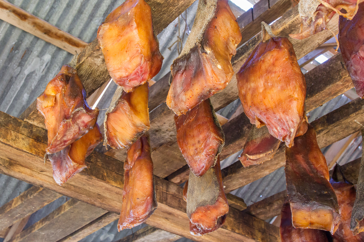 Mehrere Stücke geräuchertes Fleisch hängen zum Trocknen an Holzbalken.