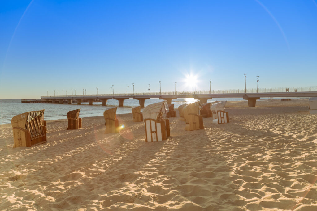 Niedrige Sonne scheint über Strandkörbe und den langen Pier am ruhigen Meer in Kolberg.