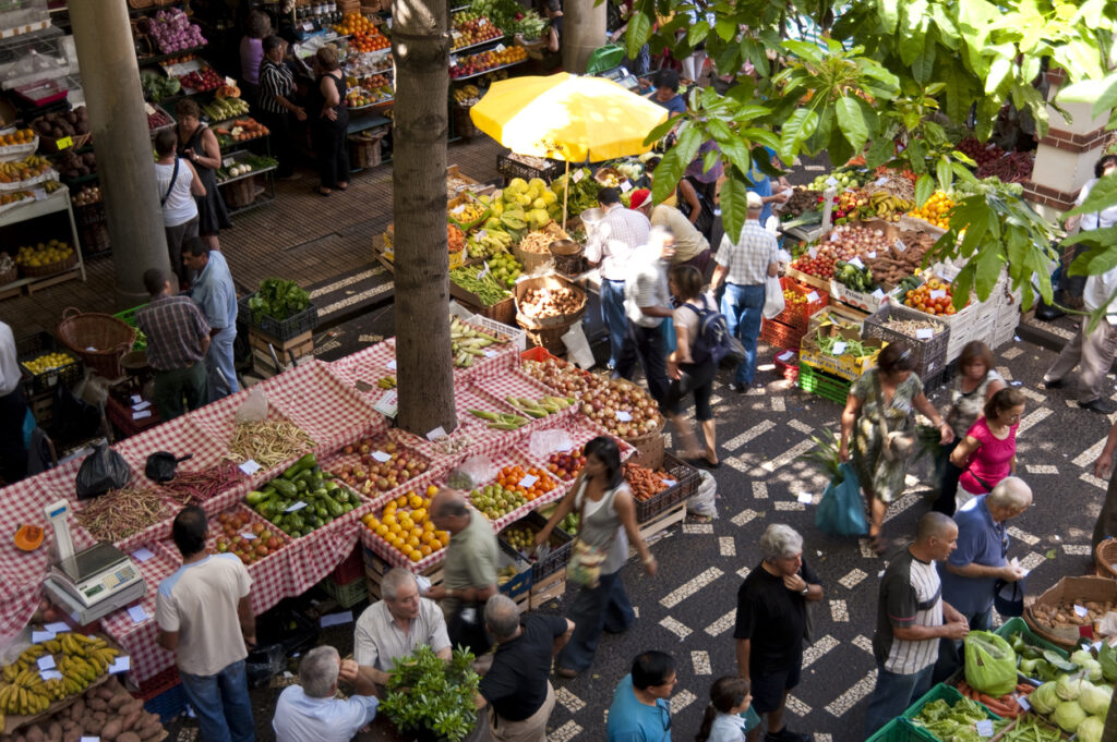 Menschen schlendern durch die Markthalle in Funchal mit bunten Obst- und Gemüseständen.