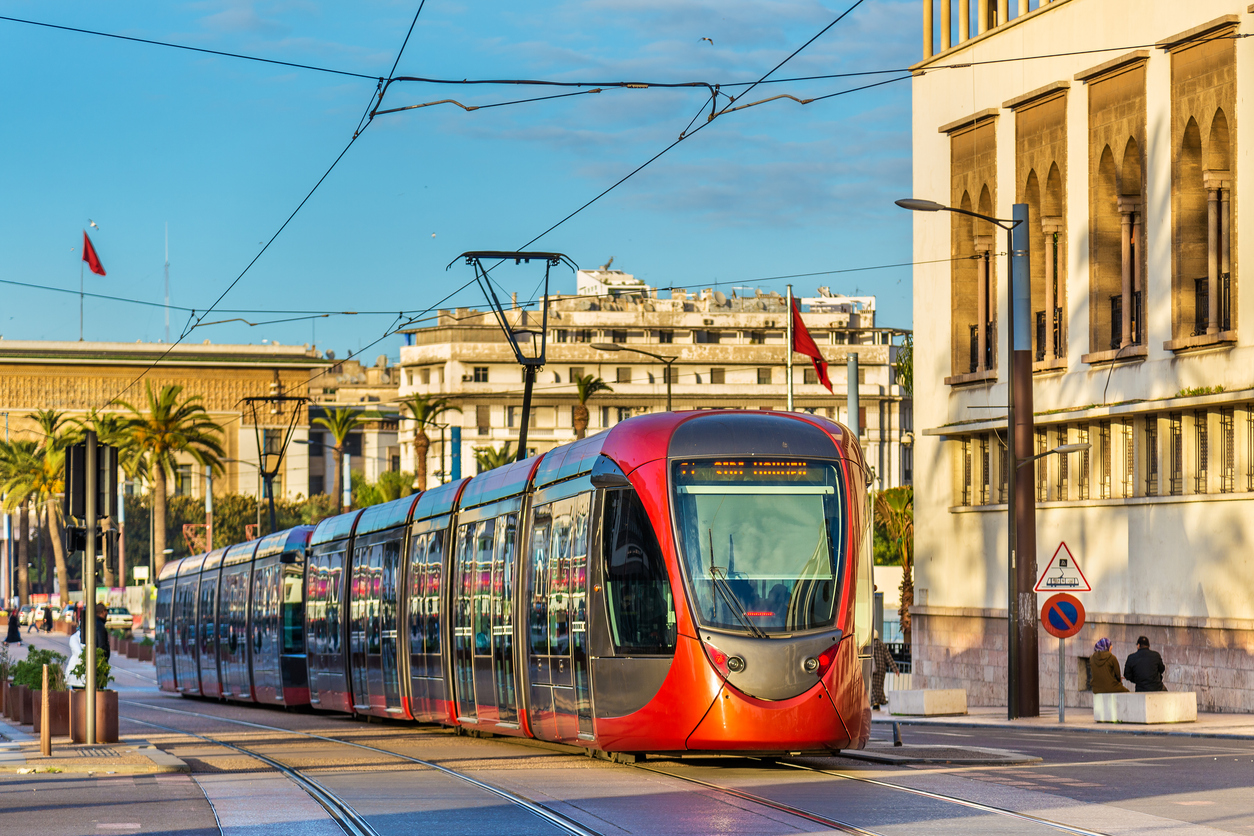 Rote Straßenbahn fährt durch Casablanca vor modernen Gebäuden und Palmen.