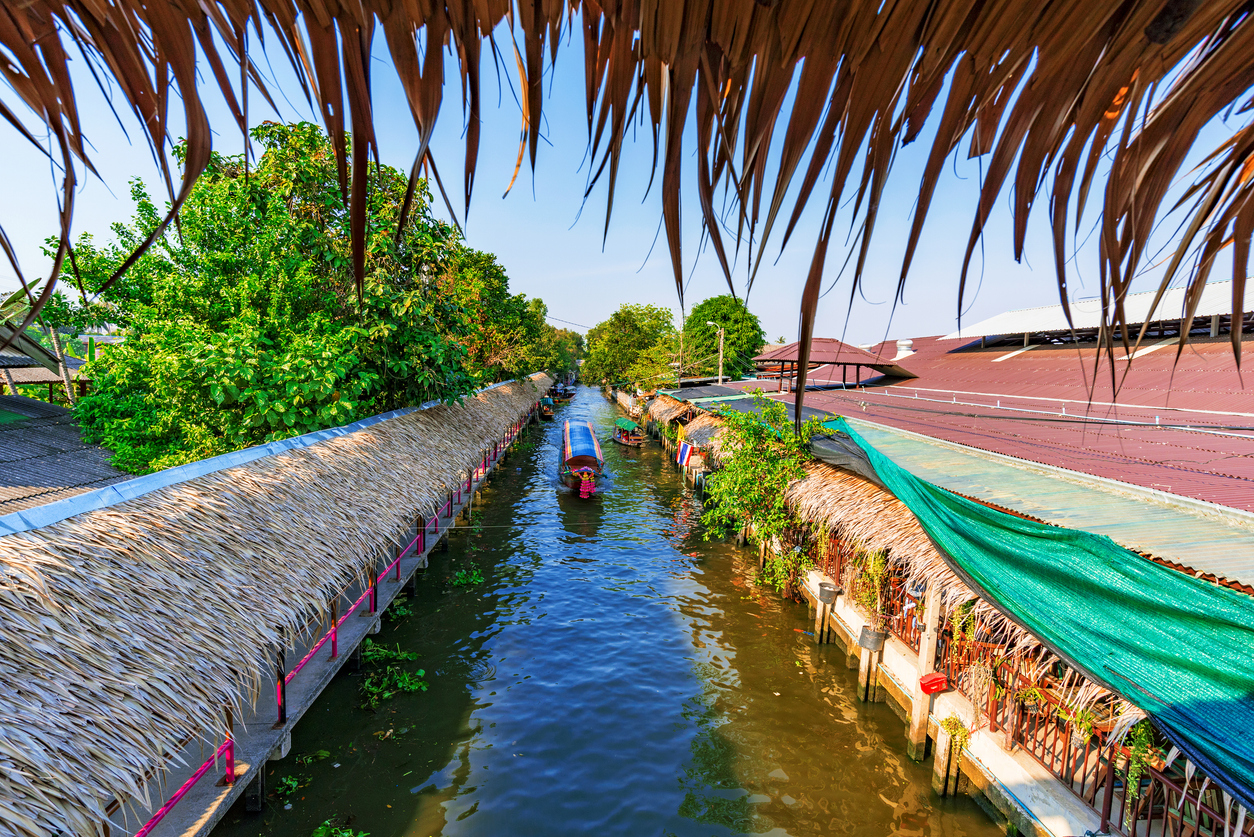 Ein Boot fährt durch den Kanal zwischen überdachten Marktständen am Khlong Lat Mayom Floating Market in Bangkok.
