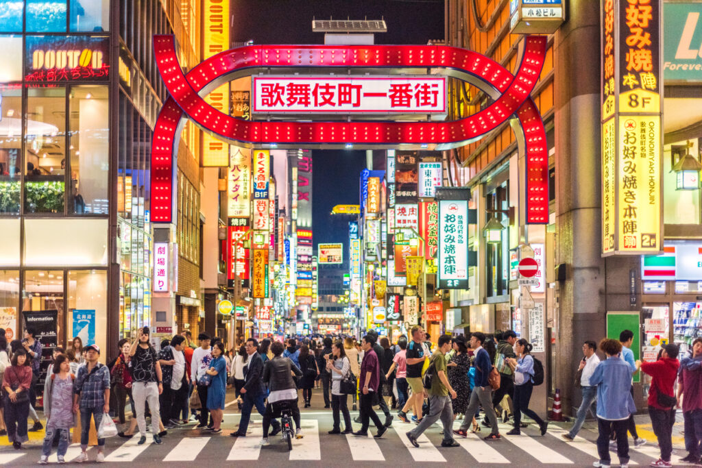 Menschen überqueren eine Straße unter dem Kabukicho Ichibangai Tor in Shinjuku, Tokyo.