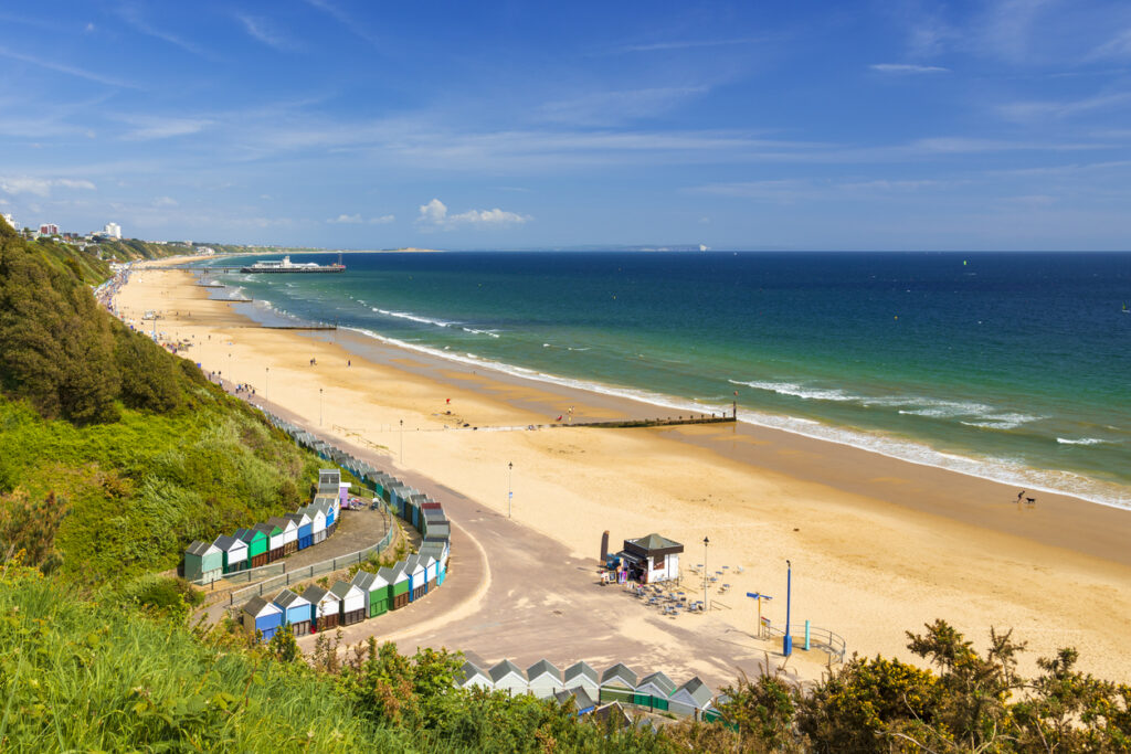 Weiter Sandstrand in Bournemouth mit Strandhütten, Promenade und blauem Meer.