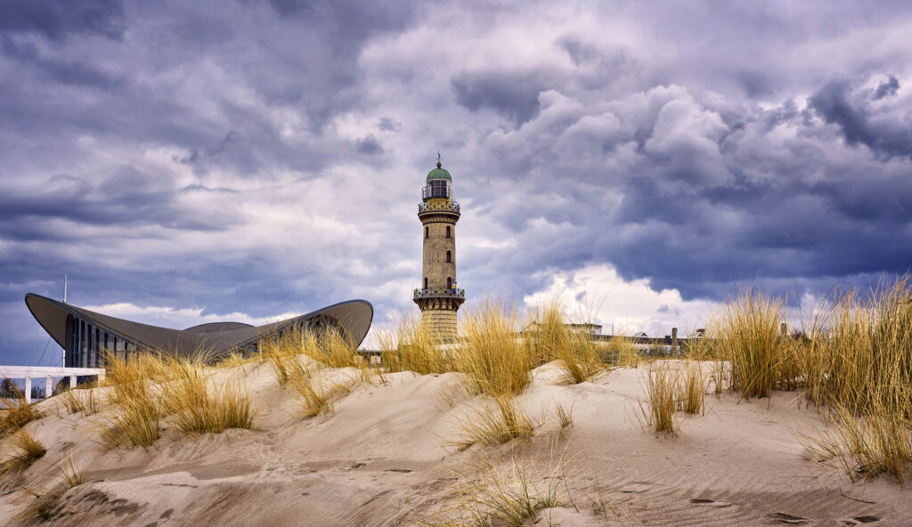 Der Leuchtturm ragt hinter den Dünen auf, dunkle Wolken ziehen dramatisch über den Himmel.