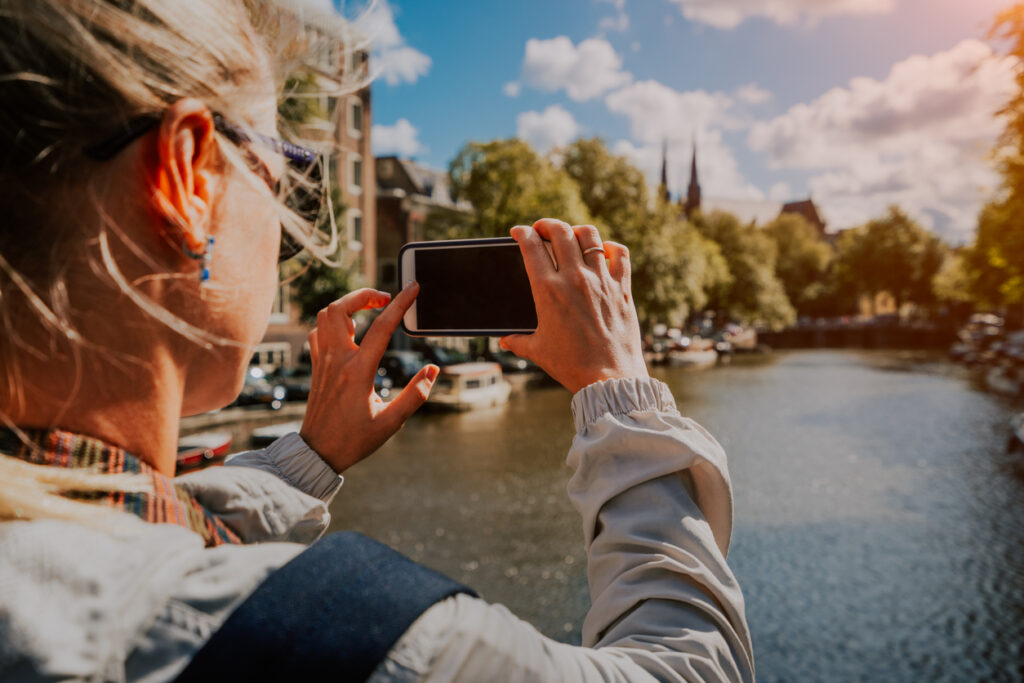 Frau fotografiert mit dem Smartphone einen Kanal in Amsterdam bei warmem Licht.