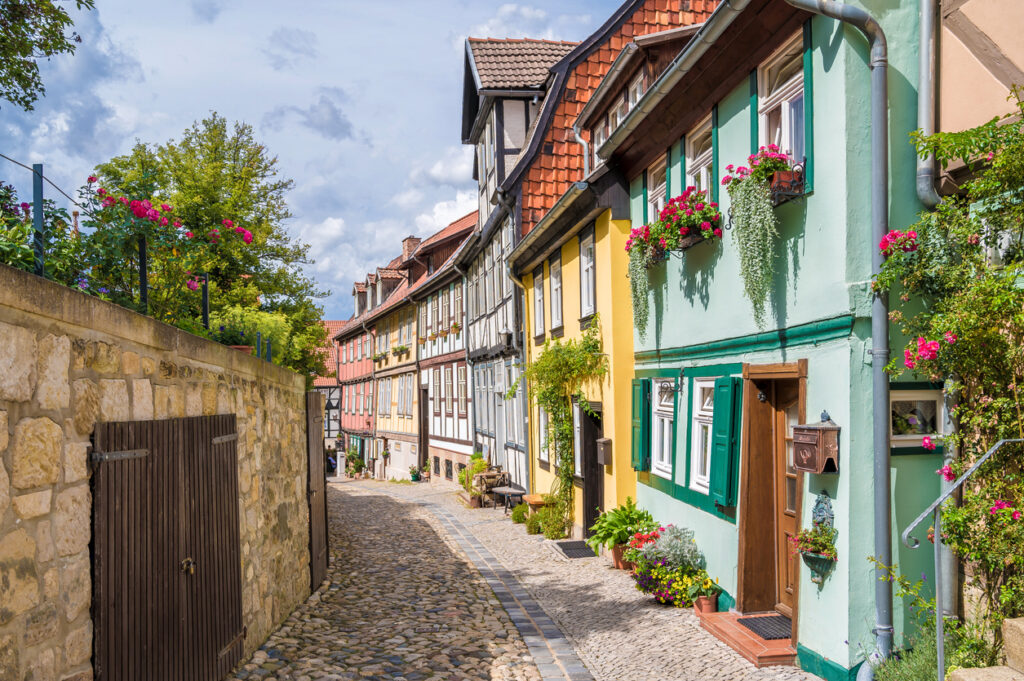 Bunte Fachwerkhäuser säumen eine schmale, gepflasterte Gasse in der Altstadt von Quedlinburg.