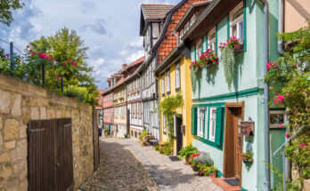 Bunte Fachwerkhäuser säumen eine schmale, gepflasterte Gasse in der Altstadt von Quedlinburg.