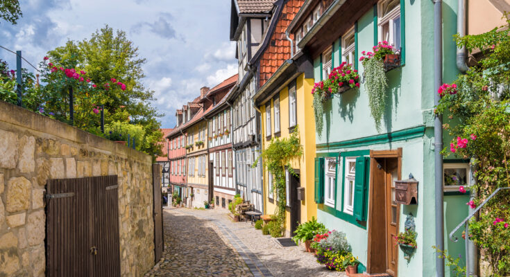 Bunte Fachwerkhäuser säumen eine schmale, gepflasterte Gasse in der Altstadt von Quedlinburg.