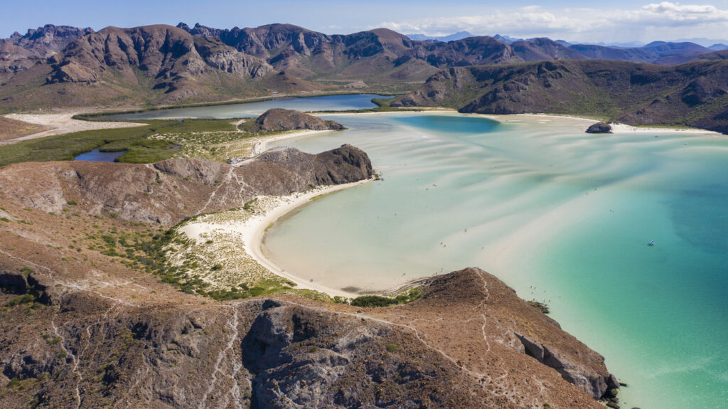Luftaufnahme einer türkisblauen Bucht mit Sandstrand und Bergen nahe La Paz in Baja California Sur.