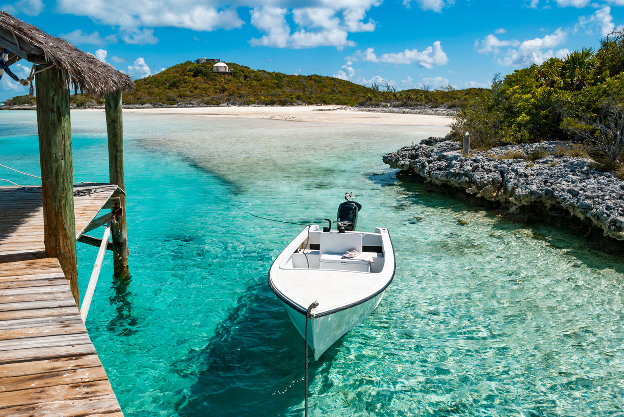 Ein Motorboot liegt an einem Steg in seichtem, transparentem Wasser vor einem ruhigen Strand.