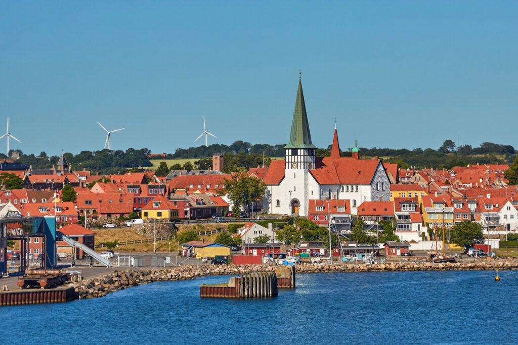Vor dem Hafen stehen Häuser mit roten Dächern und eine Kirche mit hohem Turm auf Bornholm.