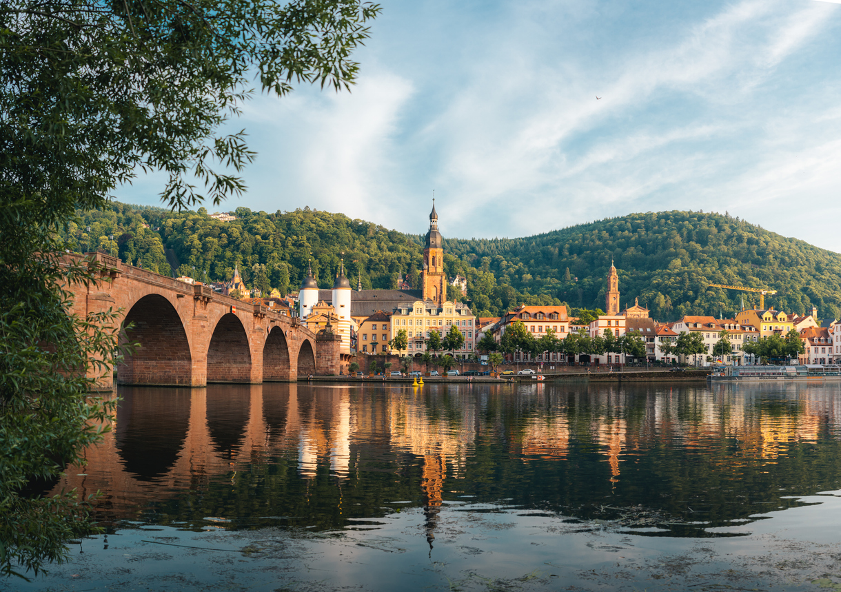 Die Bögen der Alten Brücke spiegeln sich im stillen Wasser vor der Altstadt und den bewaldeten Hängen.