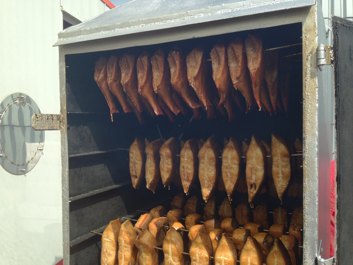 In einem geöffneten Räucherofen hängen zahlreiche Fischstücke auf mehreren Ebenen.