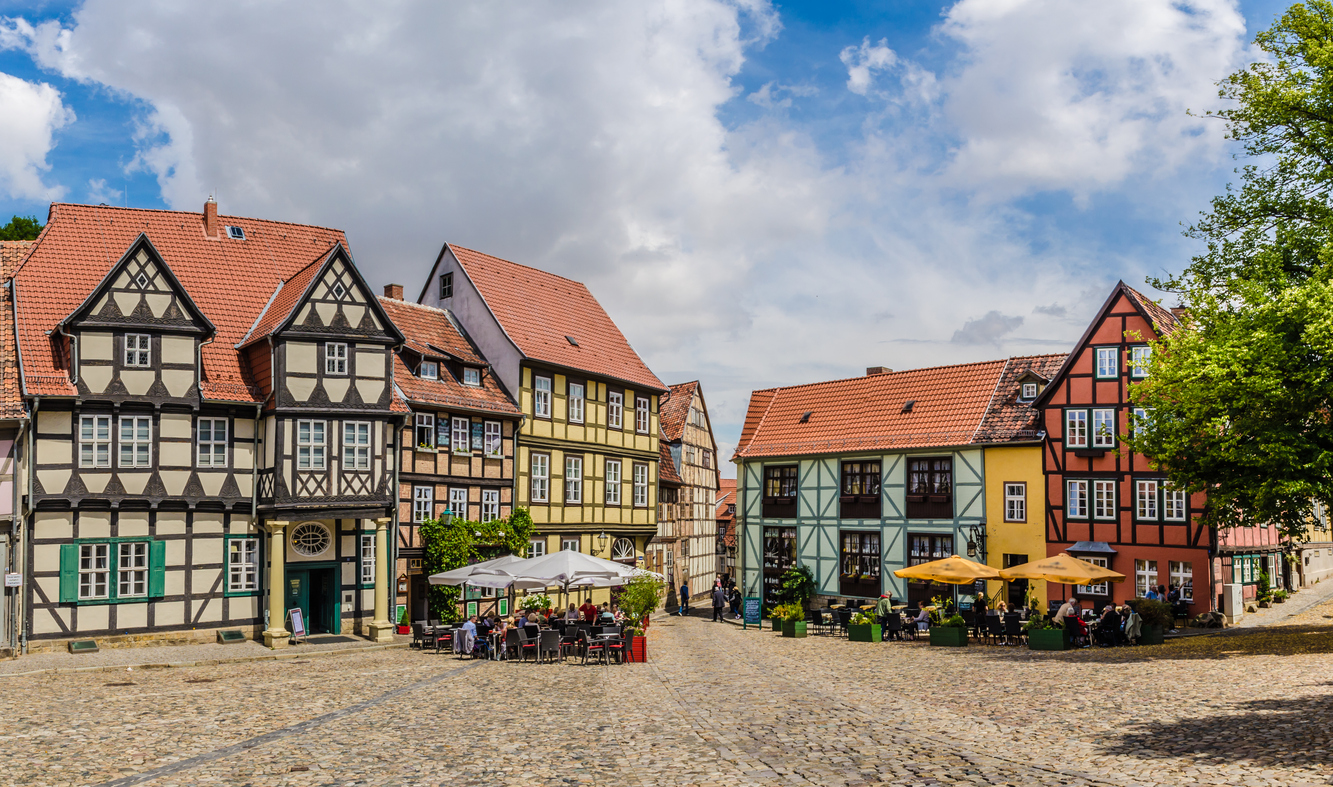 Ein Kopfsteinpflasterplatz in Quedlinburg wird von farbigen Fachwerkhäusern und Außengastronomie eingerahmt.