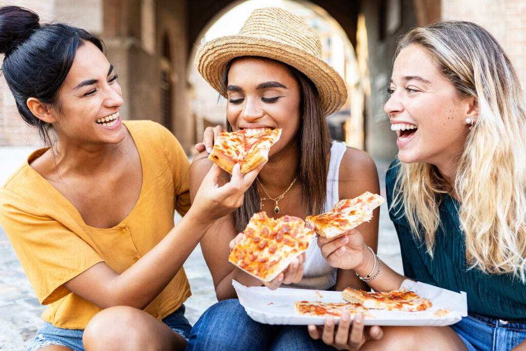 Drei Freundinnen lachen und essen Pizza zusammen in Rom.