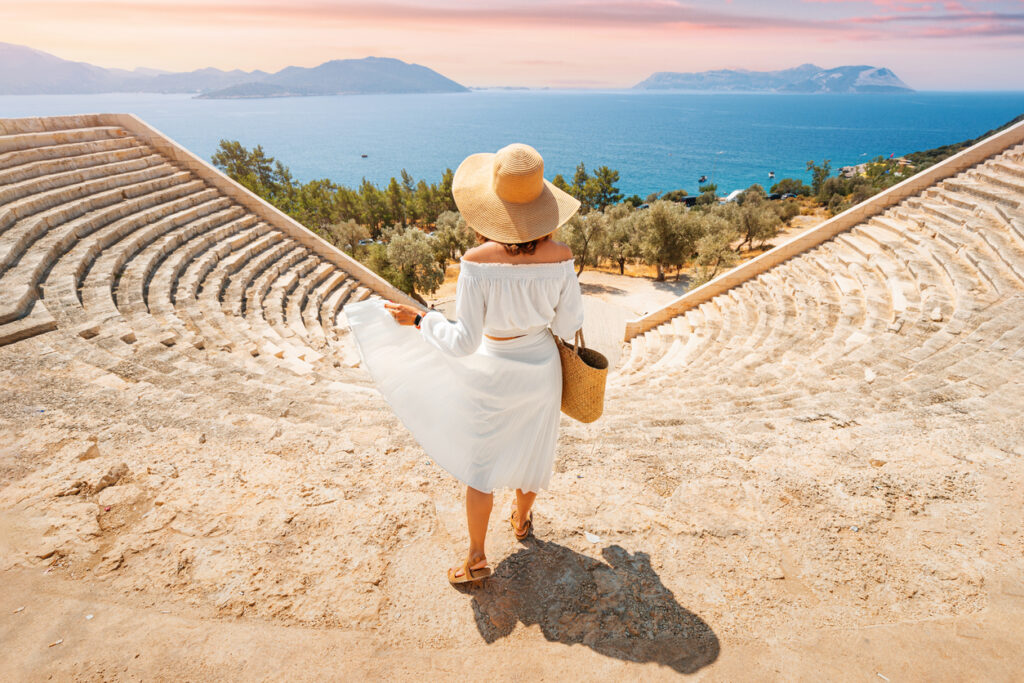 Frau im weißen Kleid steht in einem antiken Amphitheater und schaut auf das Meer nahe Rom.