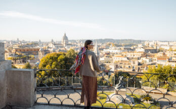 Frau steht an einem Aussichtspunkt und blickt über die Skyline von Rom.