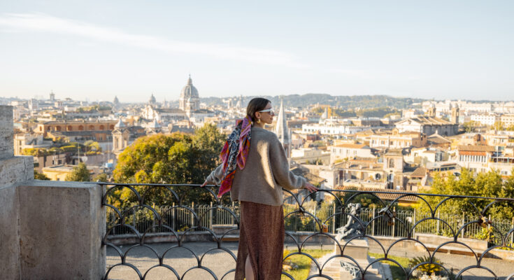 Frau steht an einem Aussichtspunkt und blickt über die Skyline von Rom.