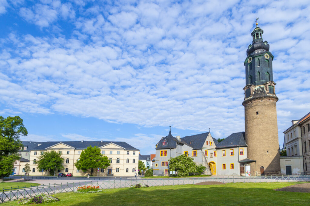 Ein hoher Turm neben historischen Gebäuden vor einem weiten Himmel mit vielen Wolken.