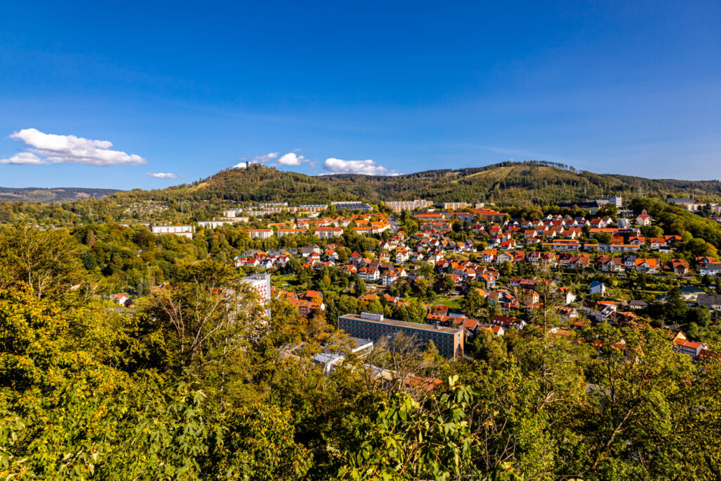 Panorama über Oberhof mit vielen roten Dächern, grünen Hügeln und blauem Himmel.