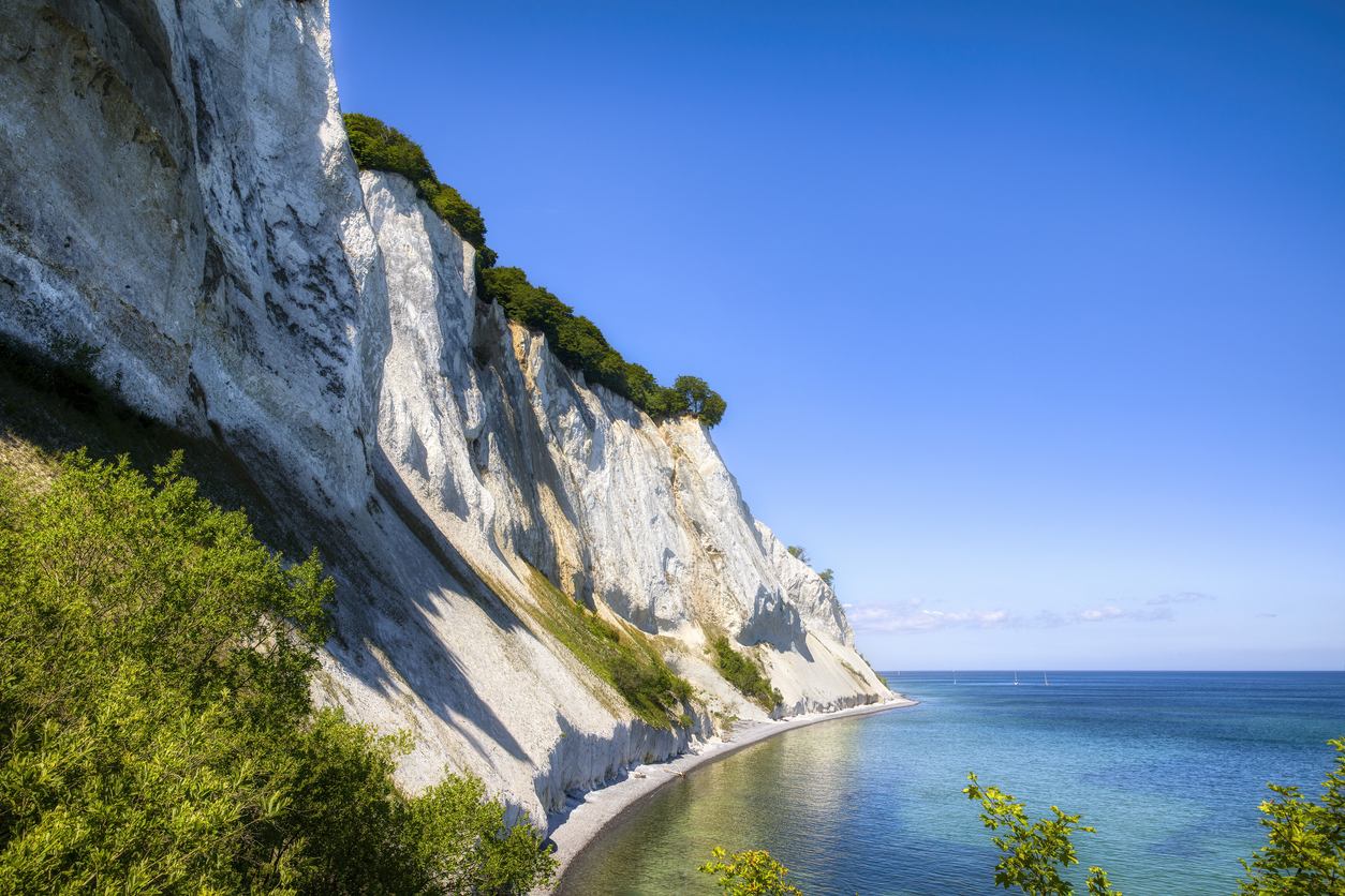 Entlang der weißen Klippen verläuft die Küste, daneben liegt spiegelglattes, tiefblaues Wasser.