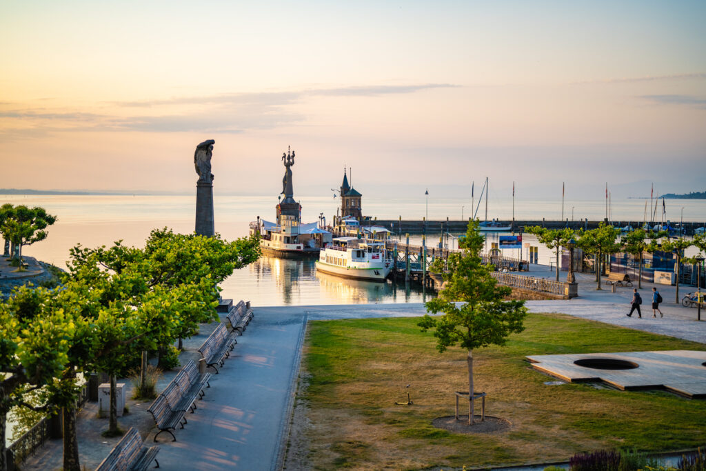 Boote liegen im Hafen, während Promenade und Wasser im weichen Morgenlicht glänzen.