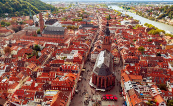 Eine Luftaufnahme zeigt dichte rote Dächer, große Kirchen und den Neckar, der sich am Stadtrand entlangzieht.