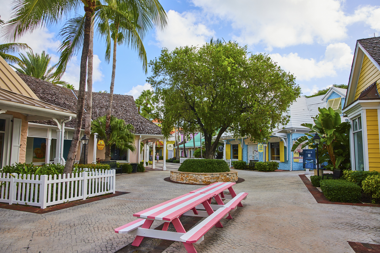 Fußgängerbereich mit pastellfarbenen Häusern, Palmen und einer rosa Sitzbank in der Mitte.