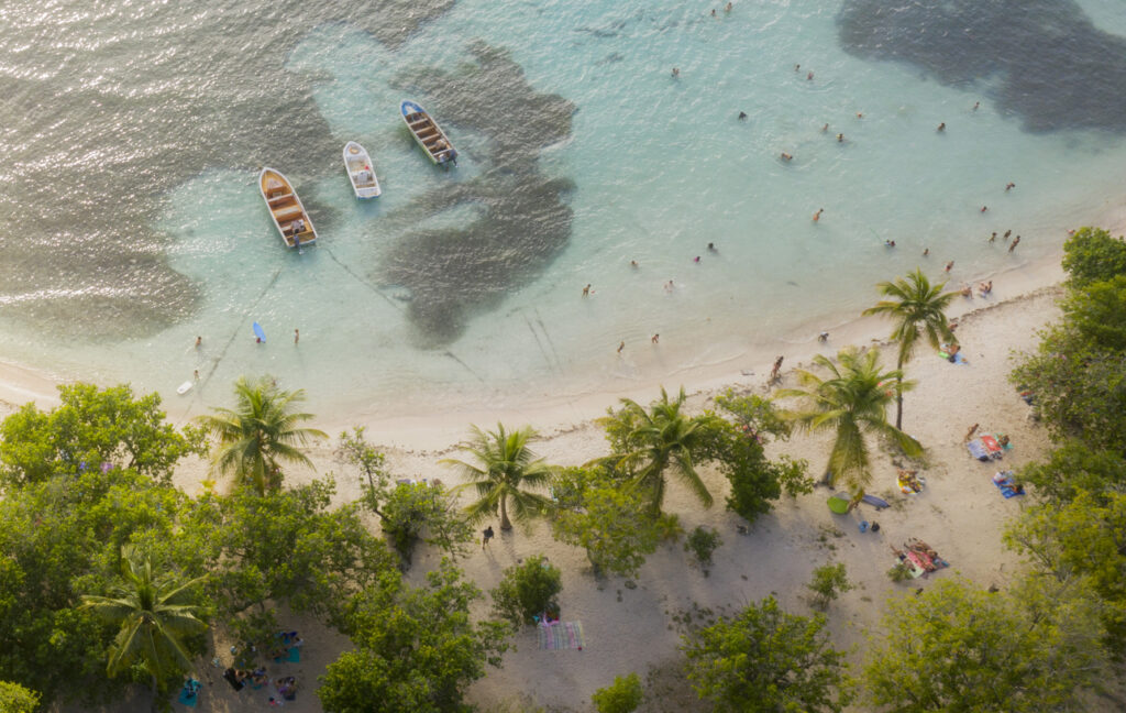 Von oben sieht man eine helle Bucht mit kleinen Booten und badenden Menschen.