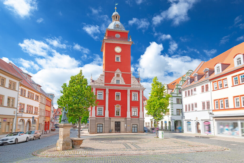 Blick auf den Marktplatz mit dem roten Rathaus und historischen Fassaden bei blauem Himmel.