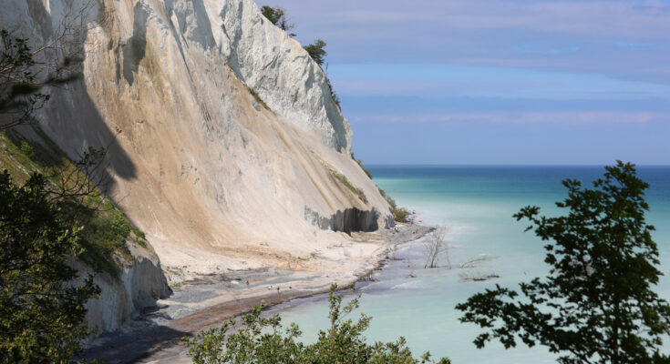 Hohe Kreideklippen fallen steil zur Küste ab, während das Meer in hellen Blaugrün-Tönen schimmert.