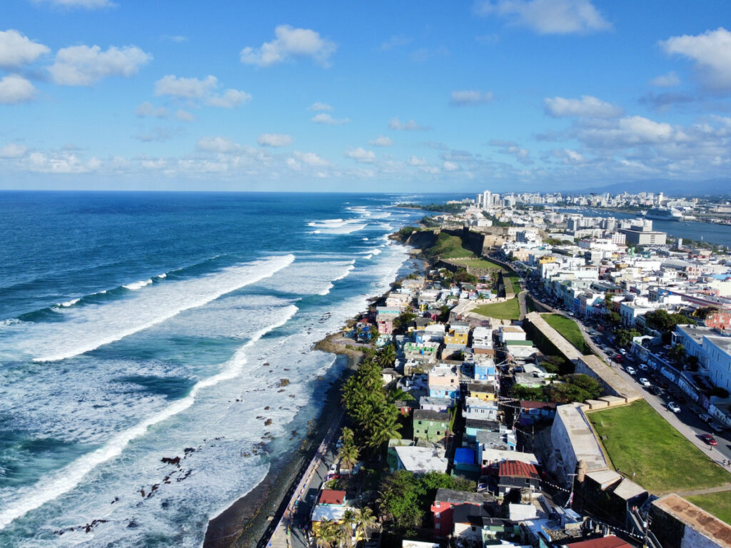 Eine lange Küstenlinie mit Wellen, Stadtvierteln und Festungsmauern am Meer in Puerto Rico.