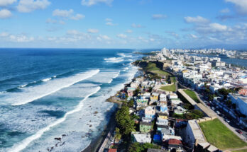 Eine lange Küstenlinie mit Wellen, Stadtvierteln und Festungsmauern am Meer in Puerto Rico.