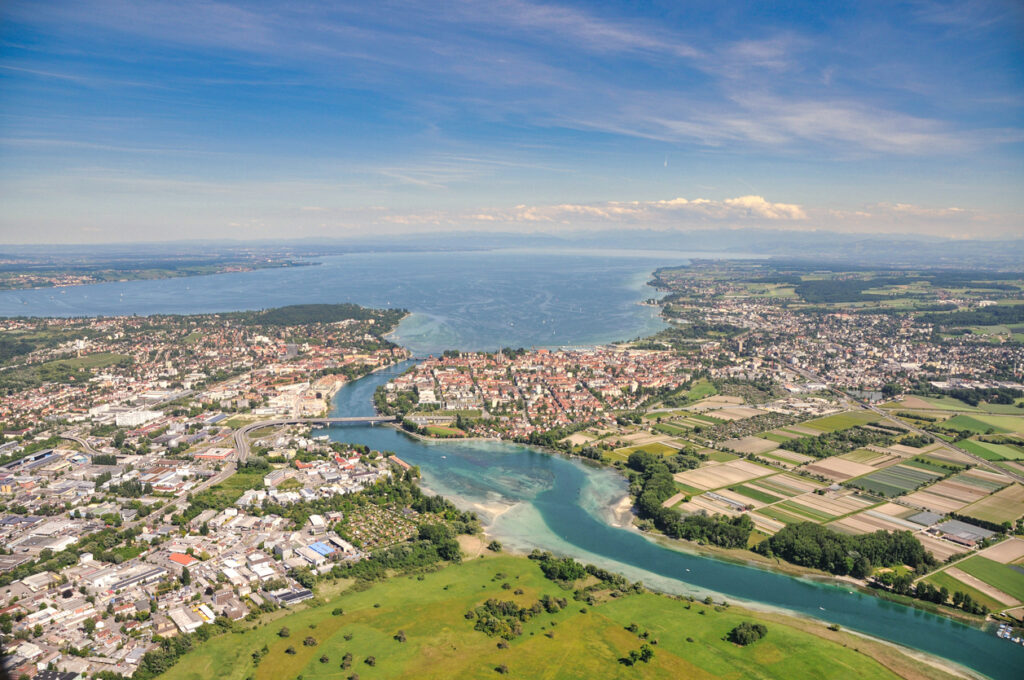 Eine Luftaufnahme zeigt Stadt, Felder und Wasserflächen, die in den See übergehen.