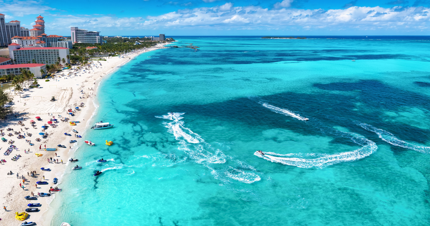 Breiter Strand mit vielen Menschen, türkisfarbenem Wasser und Hotels entlang der Küste.