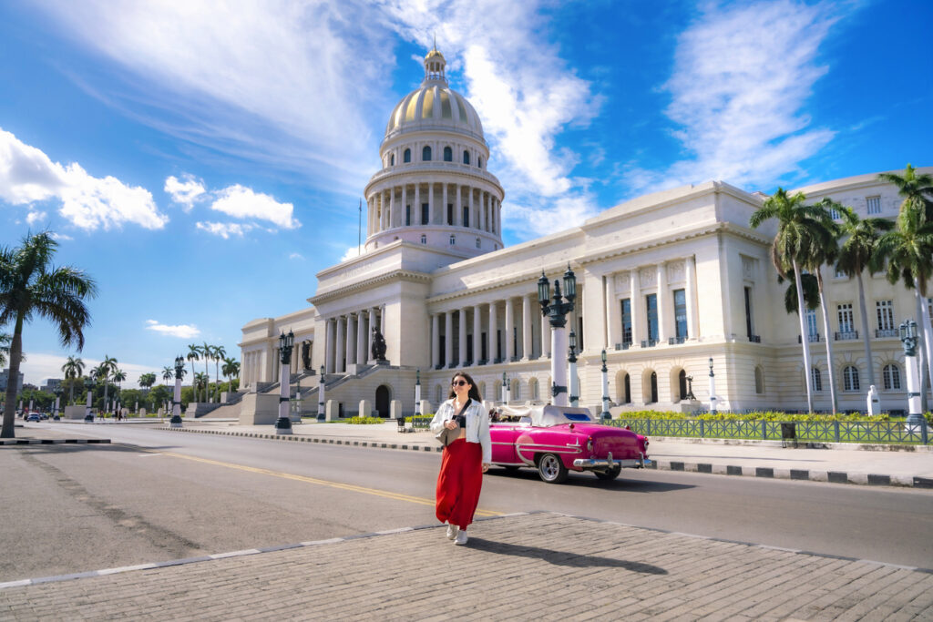 Das Capitolio in Havanna mit pinkem Oldtimer und einer Passantin im Vordergrund.
