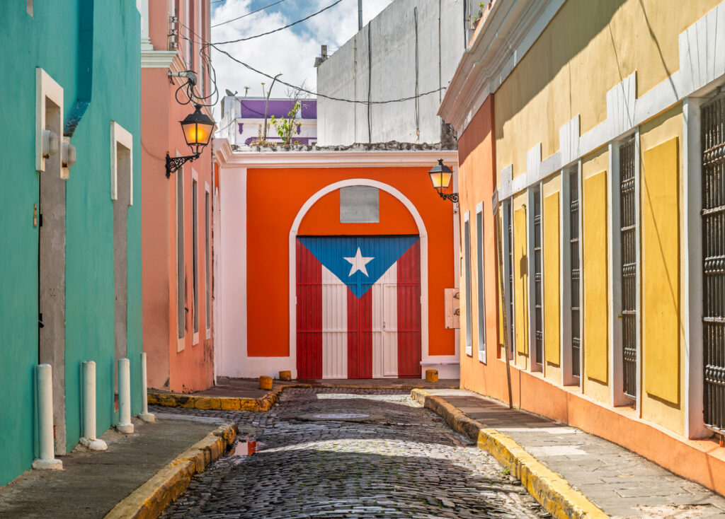 Eine Kopfsteinpflastergasse mit farbigen Häusern und einem Tor im Flaggen-Design in Puerto Rico.