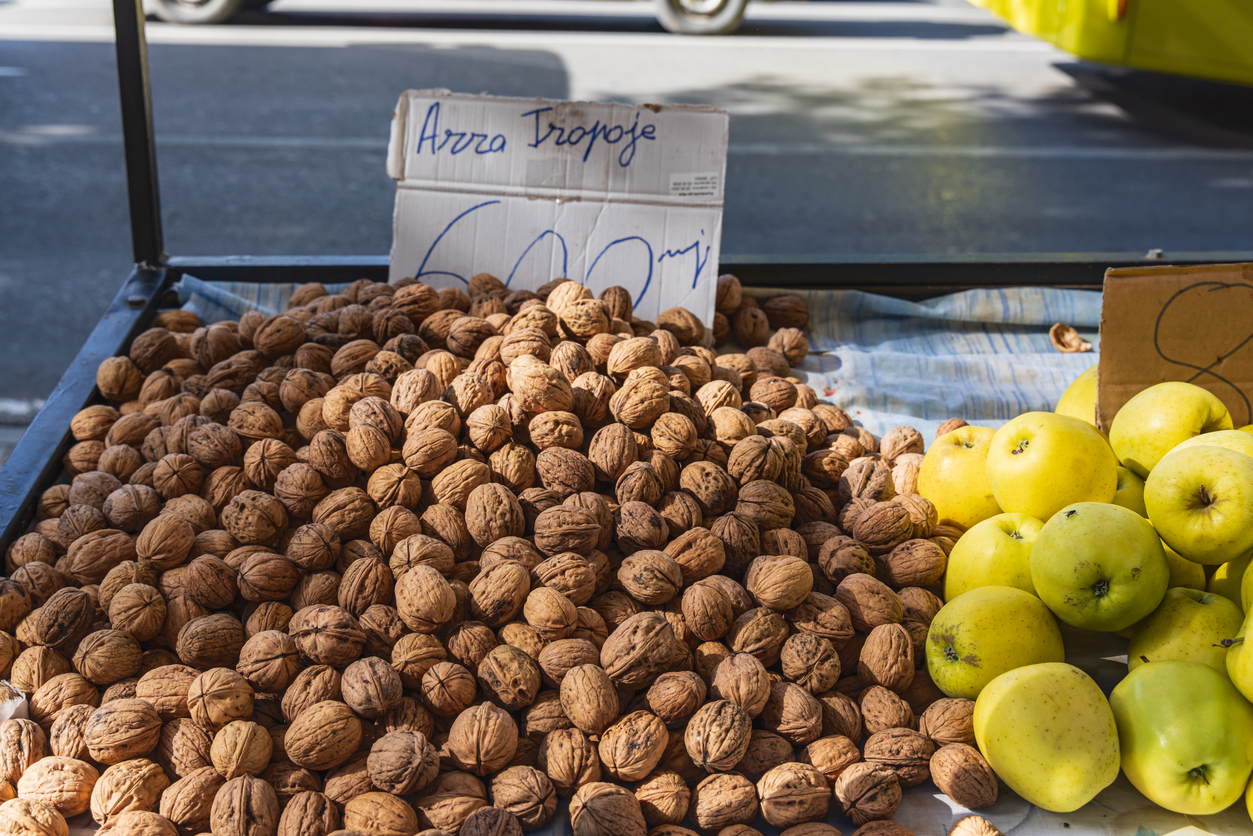 Ein Marktstand zeigt einen großen Haufen Walnüsse neben gelben Äpfeln.