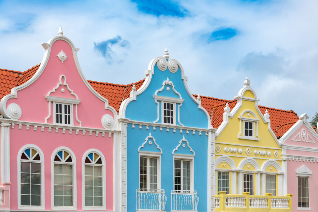 Rosa, blaue und gelbe Giebelhäuser mit roten Ziegeldächern prägen das Straßenbild auf Aruba.