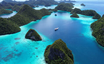 Grüne Inseln liegen in türkisblauen Lagunen, mit einem Boot im ruhigen Wasser dazwischen.