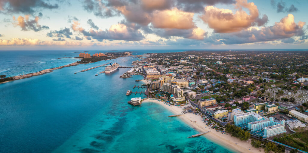 Stadt- und Hafenpanorama aus der Luft mit einem Kreuzfahrtschiff und warmen Wolkenfarben.