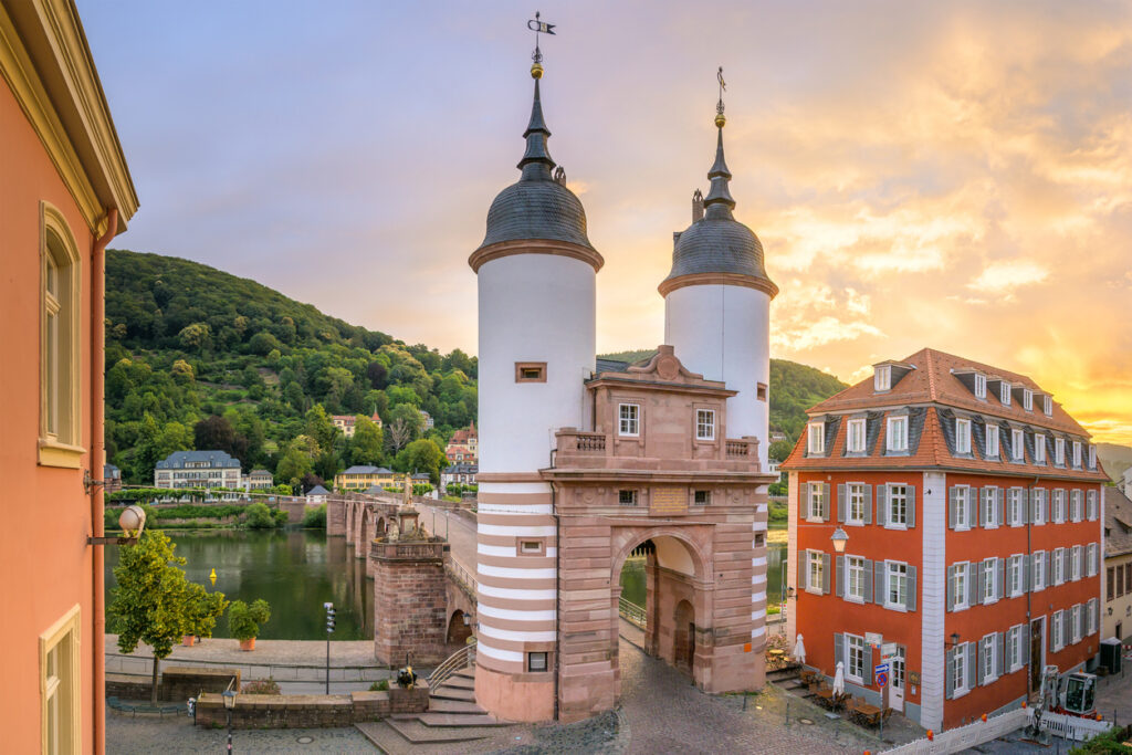 Das Brückentor mit zwei Türmen steht am Neckar und wird von warmem Sonnenuntergangslicht angestrahlt.