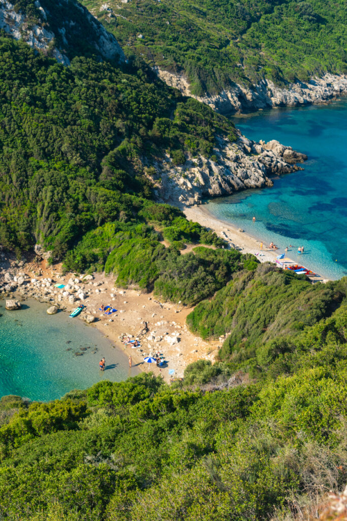 Kleine Bucht mit Kiesstrand und klarem Wasser zwischen grünen Hügeln auf Korfu.