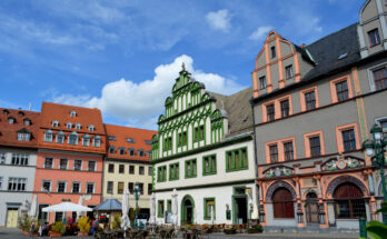 Blick auf einen Platz mit farbigen Fassaden, Außengastronomie und blauem Himmel.