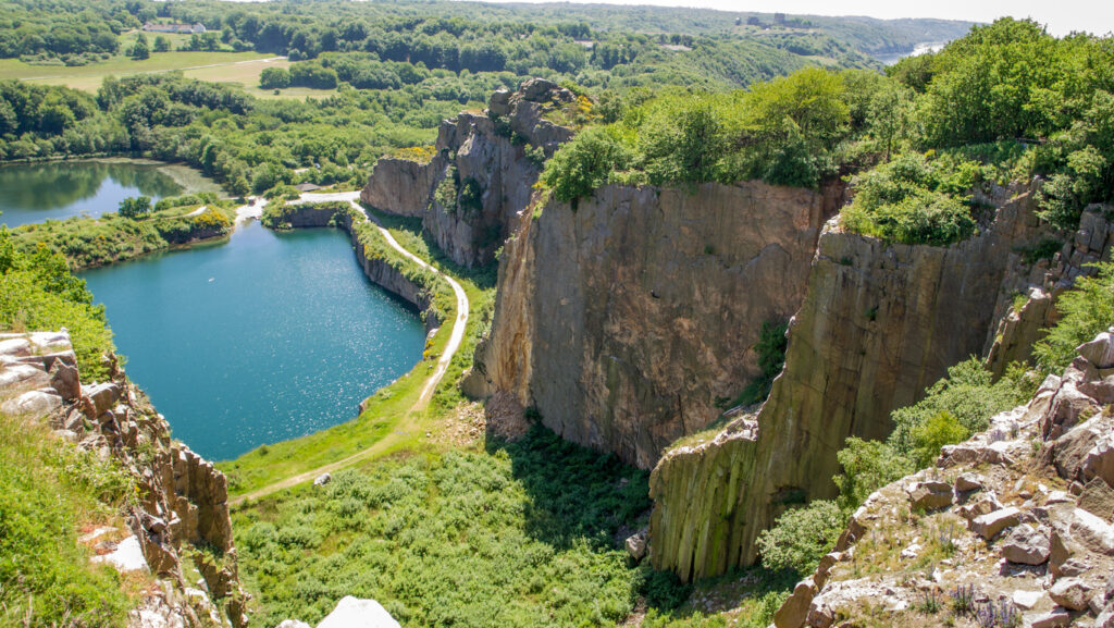 Ein türkisblauer See liegt zwischen hohen Felswänden und grünen Hängen auf Bornholm.