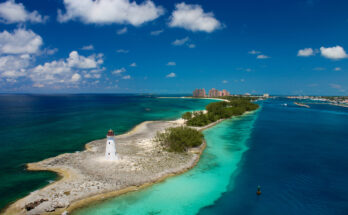 Ein weißer Leuchtturm steht auf einer sandigen Spitze zwischen tiefblauem Meer und türkisfarbener Lagune.