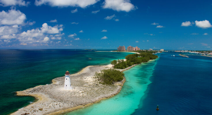 Ein weißer Leuchtturm steht auf einer sandigen Spitze zwischen tiefblauem Meer und türkisfarbener Lagune.